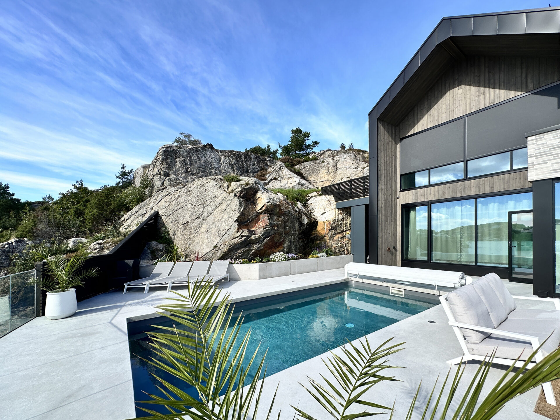 Støpt betongterrasse med integrert svømmebasseng mot naturlig fjellformasjon - omfattende betong- og murerarbeid i Kristiansand kystlandskap